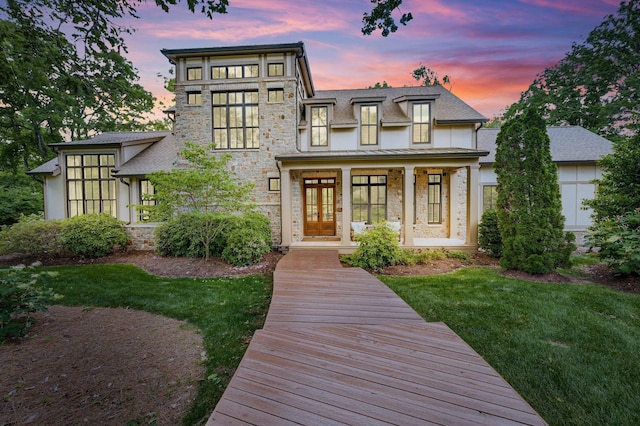 view of front of property with a lawn, stone siding, covered porch, french doors, and stucco siding