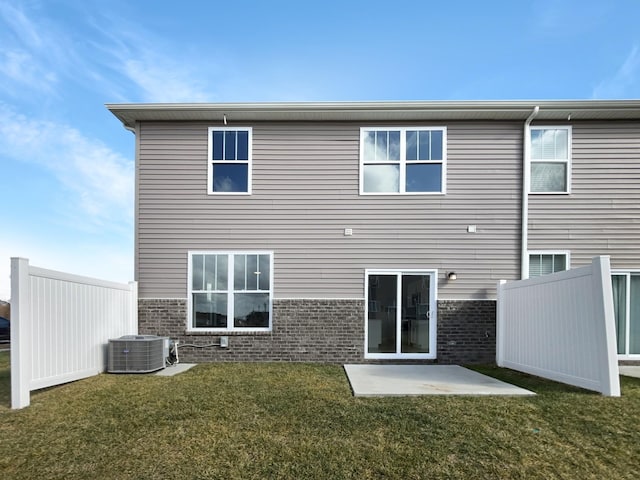 back of property with a yard, brick siding, fence, and central AC