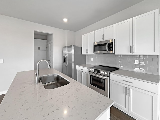 kitchen featuring light stone counters, backsplash, appliances with stainless steel finishes, white cabinetry, and a sink