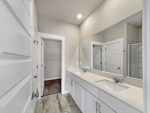 full bath featuring a sink, marble finish floor, a shower stall, double vanity, and a walk in closet