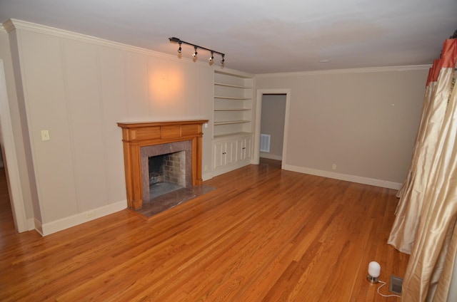 unfurnished living room with a premium fireplace, built in shelves, light wood-type flooring, crown molding, and track lighting