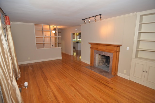 unfurnished living room with ornamental molding, built in features, hardwood / wood-style floors, and a tiled fireplace