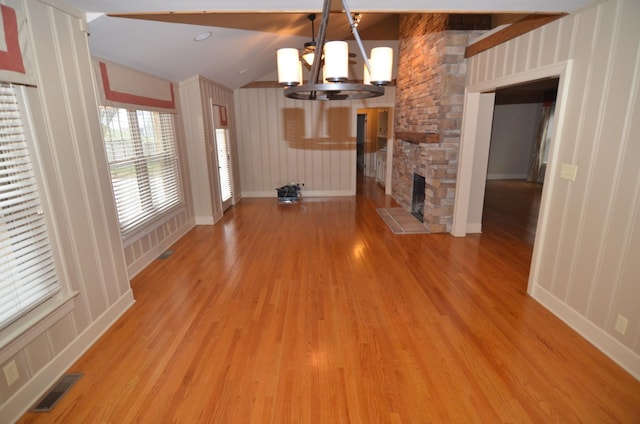 unfurnished living room featuring a fireplace, lofted ceiling, a chandelier, and light wood-type flooring