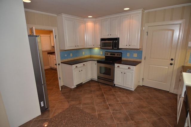 kitchen featuring appliances with stainless steel finishes, backsplash, white cabinetry, dark tile patterned flooring, and crown molding