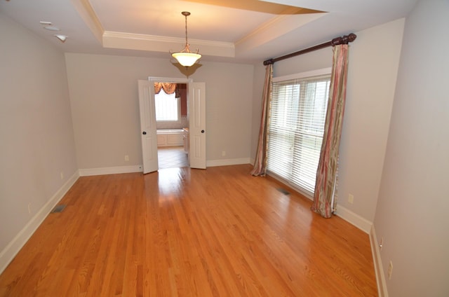 empty room with crown molding, light hardwood / wood-style floors, and a raised ceiling