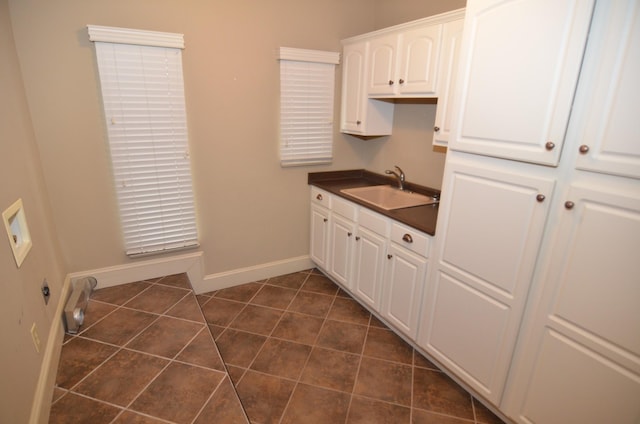 kitchen with dark tile patterned flooring, white cabinetry, and sink