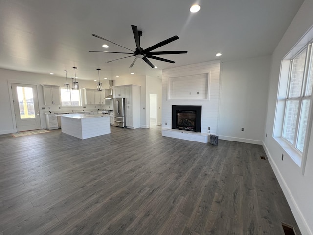 unfurnished living room featuring a large fireplace, dark wood-type flooring, and ceiling fan