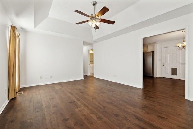 unfurnished room featuring a tray ceiling, baseboards, dark wood-type flooring, and ceiling fan with notable chandelier