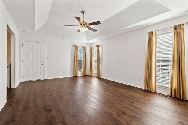 unfurnished room featuring baseboards, visible vents, a ceiling fan, a raised ceiling, and dark wood-type flooring