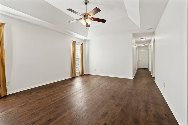 spare room with dark wood-style floors, a tray ceiling, and baseboards