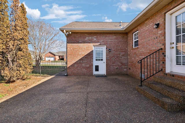 exterior space with a patio area, a shingled roof, fence, and brick siding