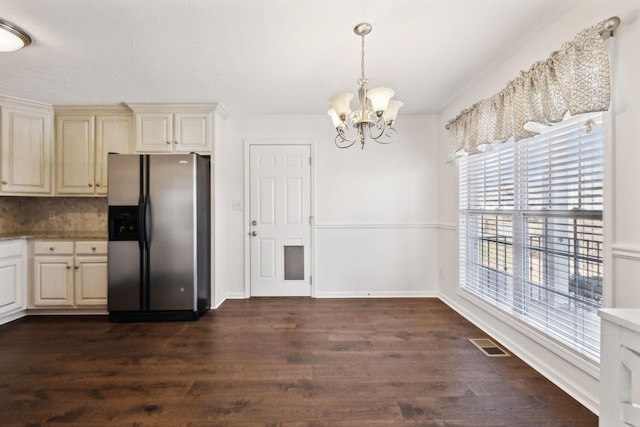 kitchen featuring stainless steel refrigerator with ice dispenser, backsplash, cream cabinets, an inviting chandelier, and dark wood-type flooring