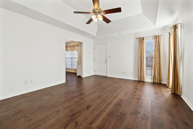 spare room featuring dark wood-style floors, a tray ceiling, and baseboards