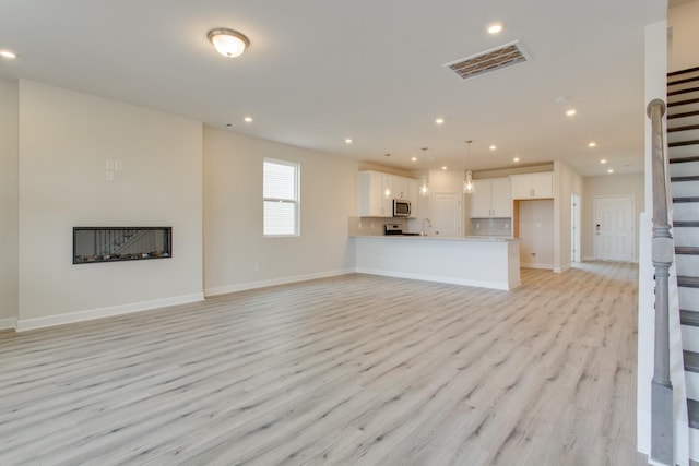 unfurnished living room with stairway, visible vents, and recessed lighting