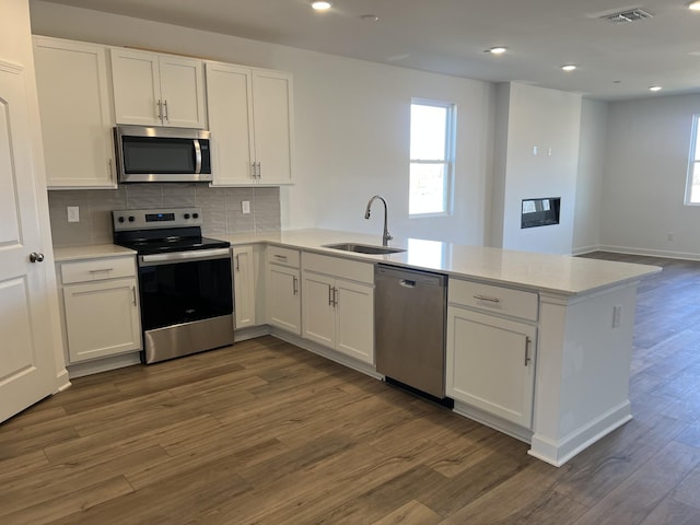 kitchen featuring stainless steel appliances, a peninsula, a sink, white cabinets, and dark wood-style floors