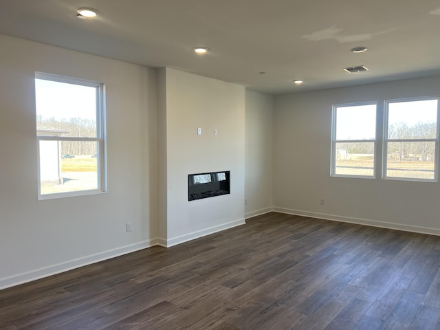 unfurnished living room with recessed lighting, baseboards, dark wood finished floors, and a glass covered fireplace