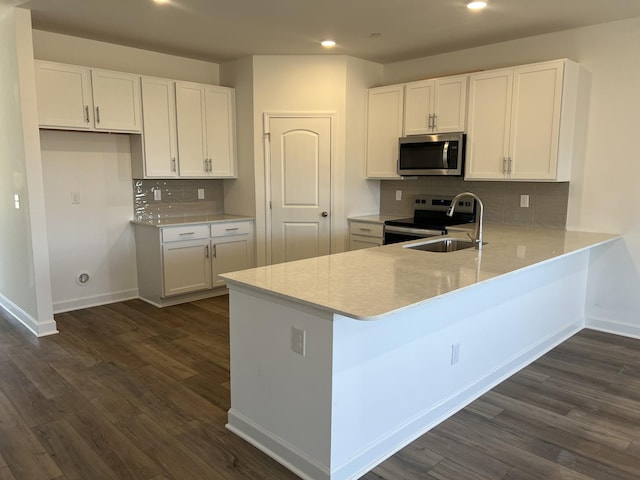 kitchen featuring a peninsula, dark wood-type flooring, a sink, white cabinets, and appliances with stainless steel finishes