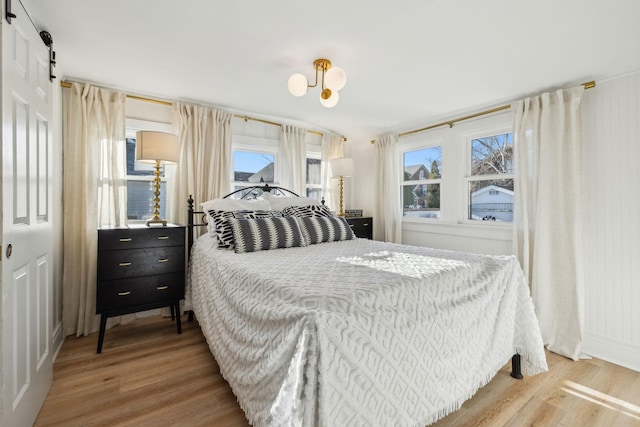 bedroom featuring hardwood / wood-style flooring, a barn door, and a chandelier