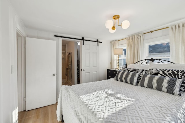 bedroom featuring a notable chandelier, light hardwood / wood-style floors, and a barn door