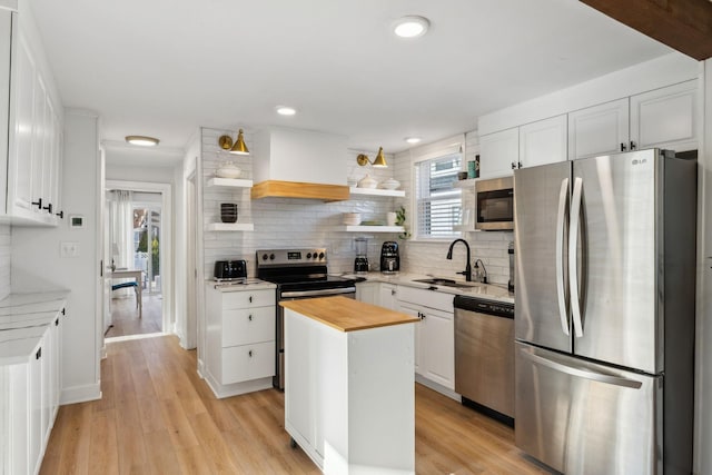 kitchen featuring white cabinetry, stainless steel appliances, a kitchen island, sink, and wood counters