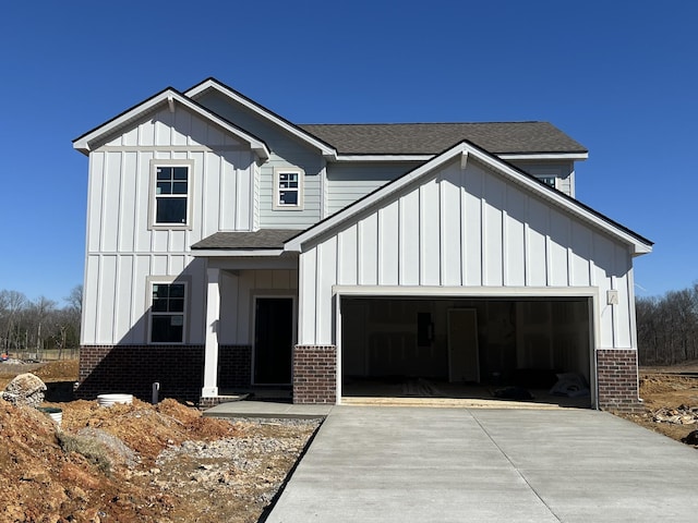 modern farmhouse style home featuring an attached garage, brick siding, a shingled roof, concrete driveway, and board and batten siding