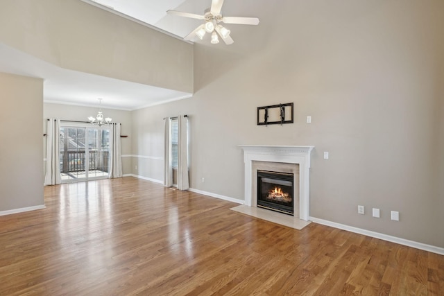 unfurnished living room featuring ceiling fan with notable chandelier, light hardwood / wood-style flooring, a high end fireplace, and a towering ceiling