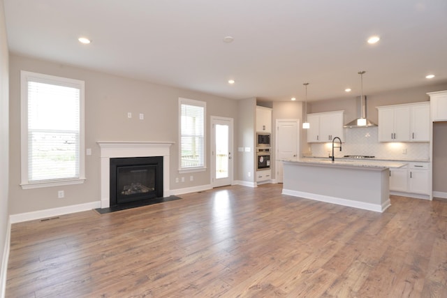 kitchen featuring appliances with stainless steel finishes, white cabinets, a kitchen island with sink, and wall chimney exhaust hood