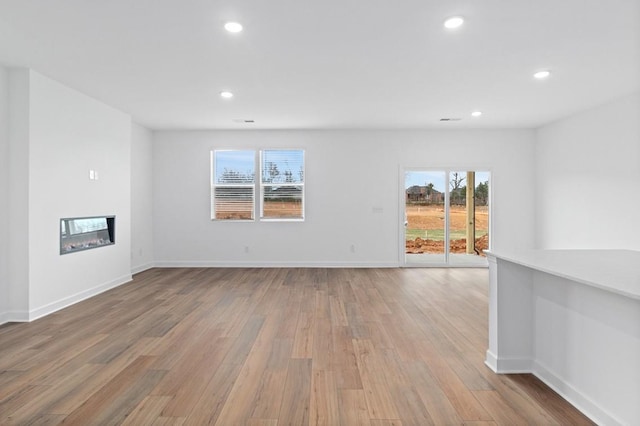 unfurnished living room with a glass covered fireplace, baseboards, light wood finished floors, and recessed lighting