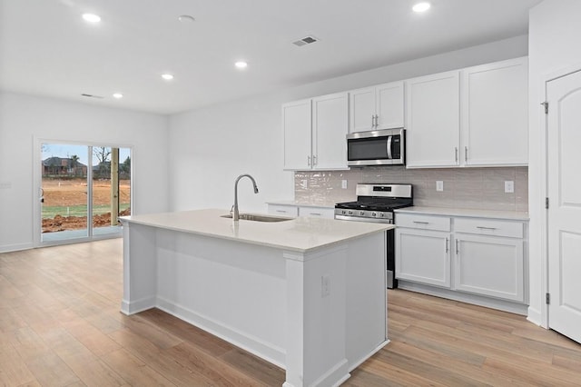 kitchen with a center island with sink, tasteful backsplash, appliances with stainless steel finishes, a sink, and light wood-type flooring