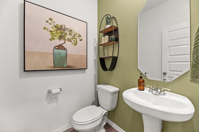 half bath featuring toilet, baseboards, and a sink