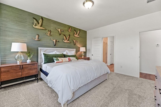 bedroom with an accent wall, carpet, visible vents, and baseboards