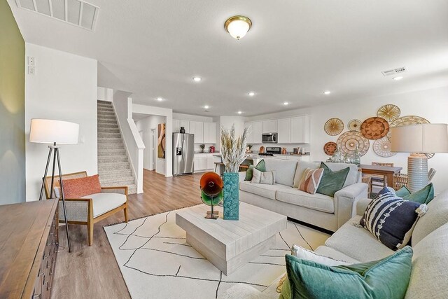 living room with light wood-type flooring, stairs, visible vents, and recessed lighting