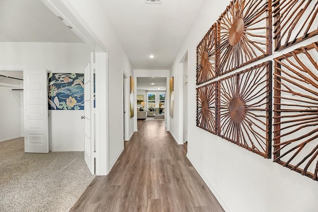 corridor with carpet floors, wood finished floors, visible vents, and baseboards