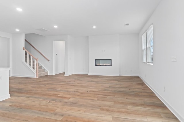 unfurnished living room featuring light wood-style floors, recessed lighting, stairway, and a glass covered fireplace