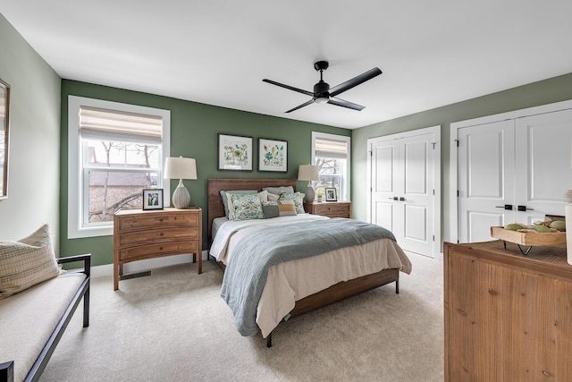 bedroom with ceiling fan, multiple closets, and light colored carpet