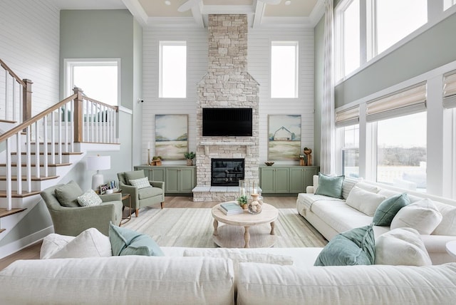 living room featuring light hardwood / wood-style flooring, a stone fireplace, and a towering ceiling