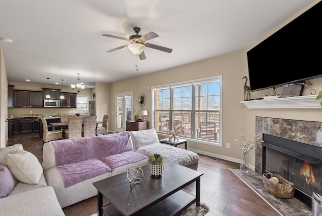 living room with dark hardwood / wood-style flooring, a high end fireplace, and ceiling fan with notable chandelier