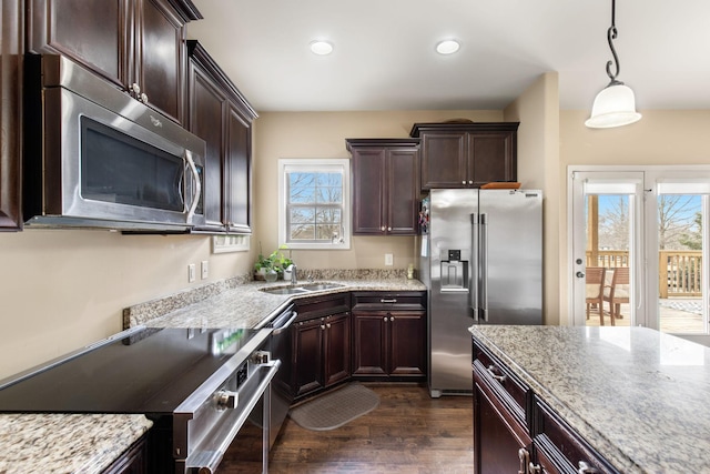 kitchen featuring sink, light stone counters, dark wood-type flooring, appliances with stainless steel finishes, and pendant lighting