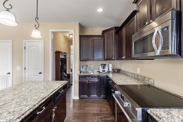 kitchen featuring dark wood-type flooring, appliances with stainless steel finishes, hanging light fixtures, and light stone counters