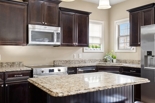 kitchen with light stone countertops, sink, stainless steel appliances, and hanging light fixtures