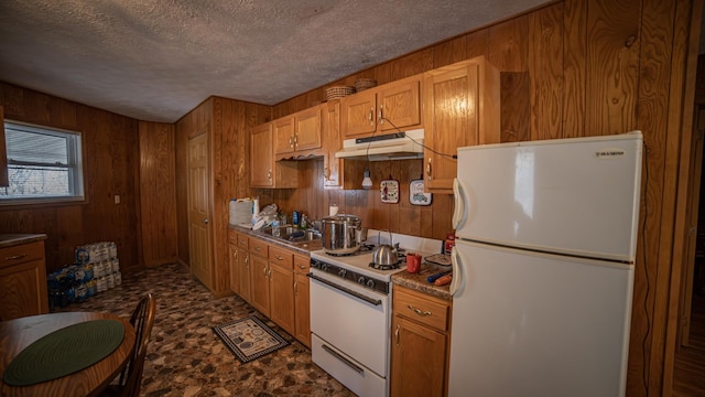 kitchen with sink, white appliances, a textured ceiling, and wood walls