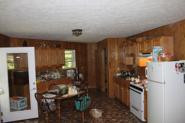 kitchen featuring a textured ceiling, white appliances, wooden walls, and range hood