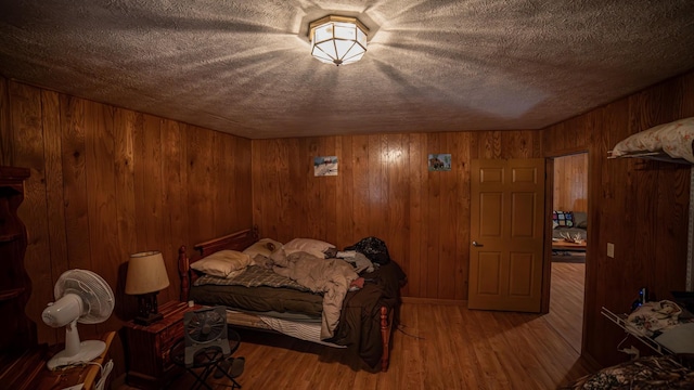 bedroom featuring a textured ceiling, hardwood / wood-style flooring, and wood walls