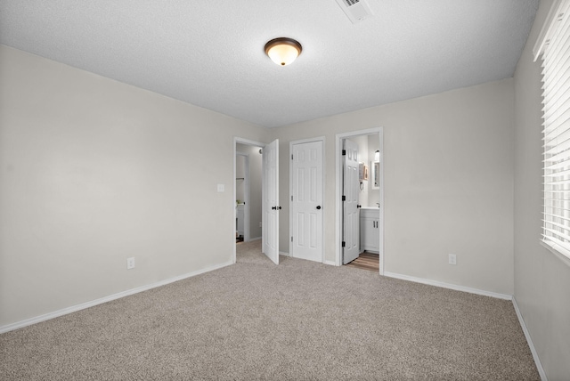 unfurnished bedroom with connected bathroom, multiple windows, a textured ceiling, and light colored carpet