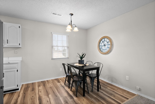 dining room with a textured ceiling, an inviting chandelier, and light hardwood / wood-style flooring