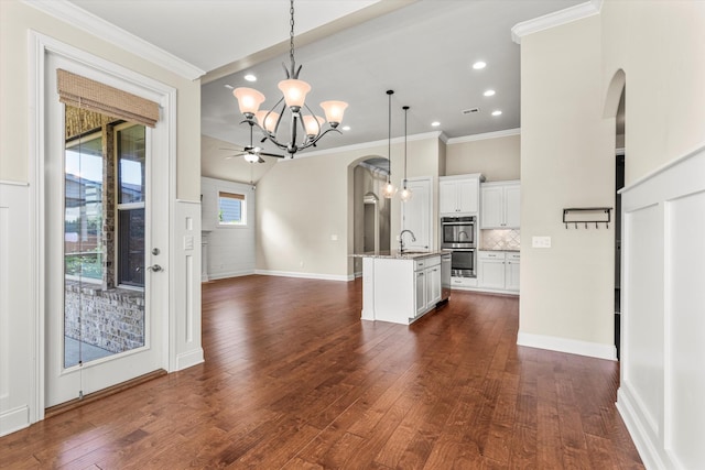 kitchen with double oven, sink, decorative light fixtures, white cabinets, and a kitchen island with sink