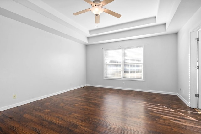 empty room with a tray ceiling, ceiling fan, and dark wood-type flooring