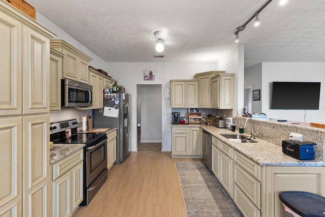 kitchen featuring appliances with stainless steel finishes, light wood-type flooring, cream cabinets, backsplash, and sink