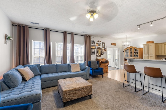 living room featuring a textured ceiling, light carpet, track lighting, and ceiling fan with notable chandelier