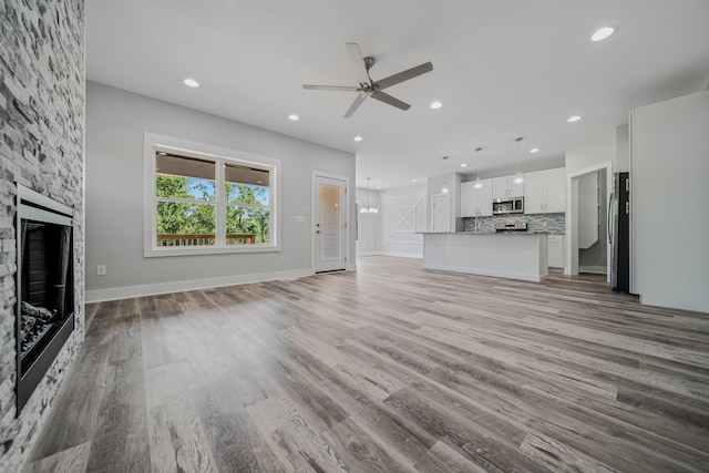 unfurnished living room with ceiling fan, a stone fireplace, and light hardwood / wood-style flooring